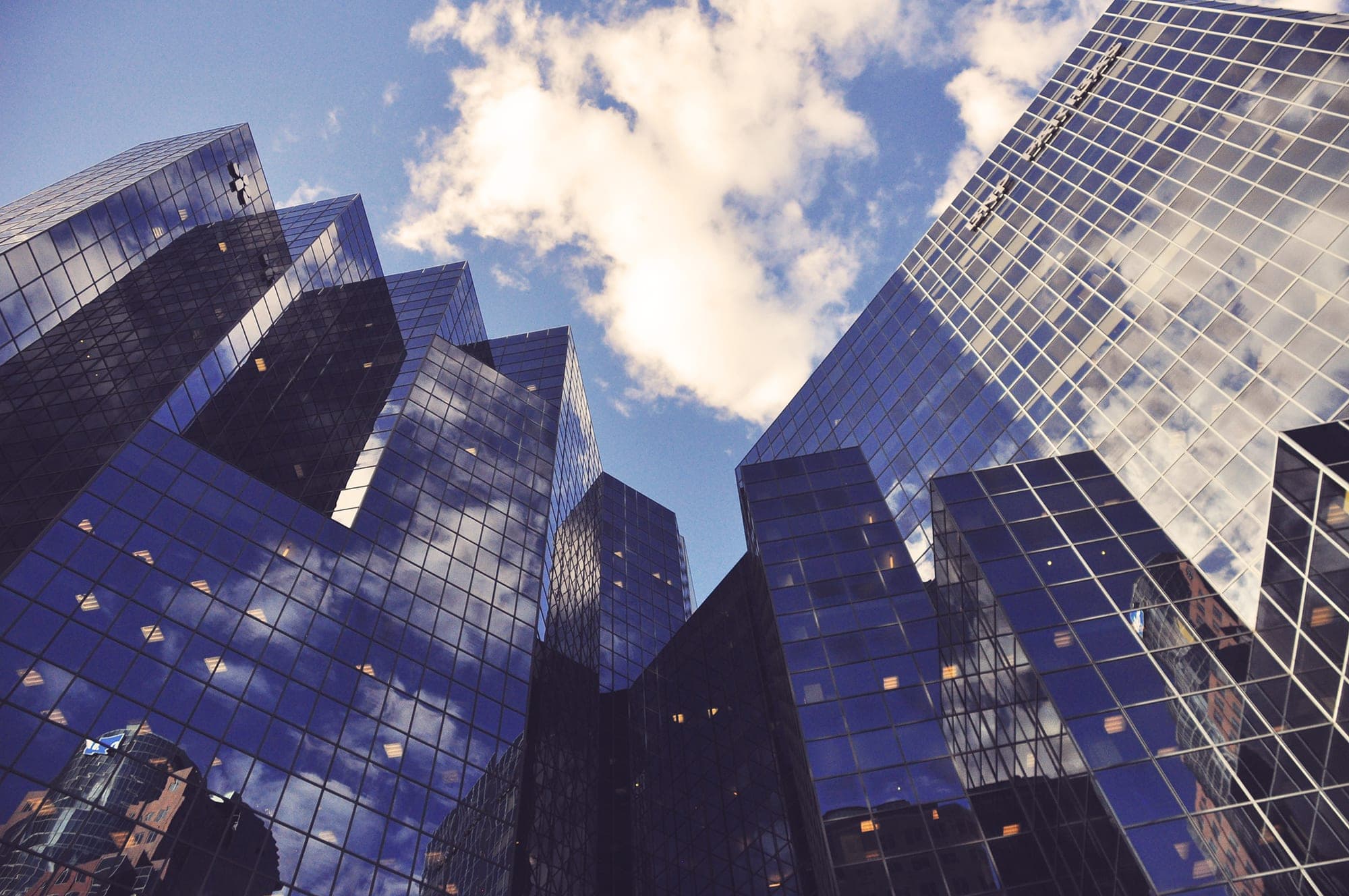 Glass office towers seen looking straight up, sky reflected across the facades